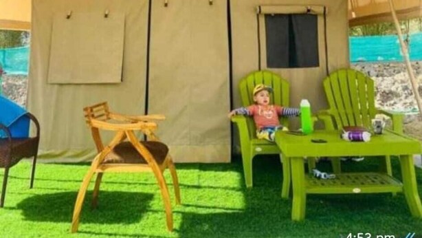 Una carpa con una puerta y una ventana, una mesita, dos sillas y una botella en el suelo.