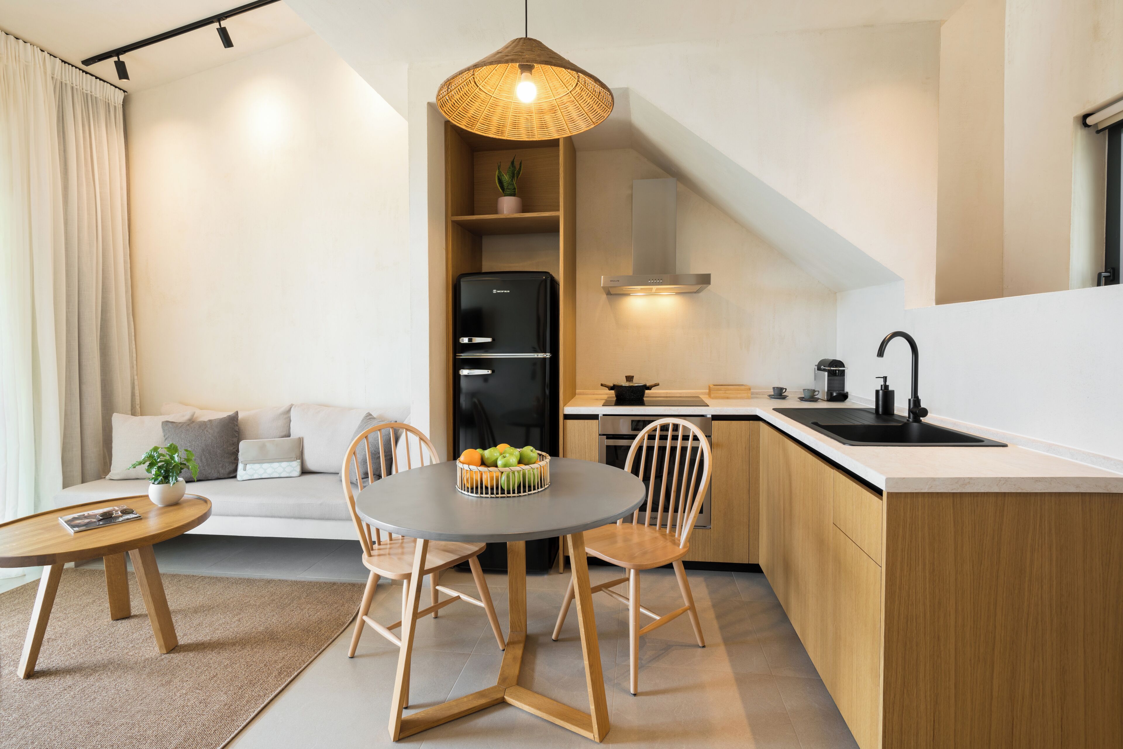 Cocina compacta con comedor, refrigerador negro, armarios de madera y una lámpara colgante.