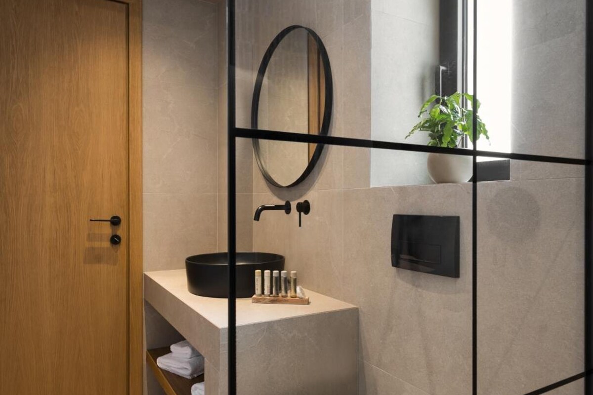 A modern bathroom with a wooden door, a black sink, a white toilet, and a mirror on the wall.
