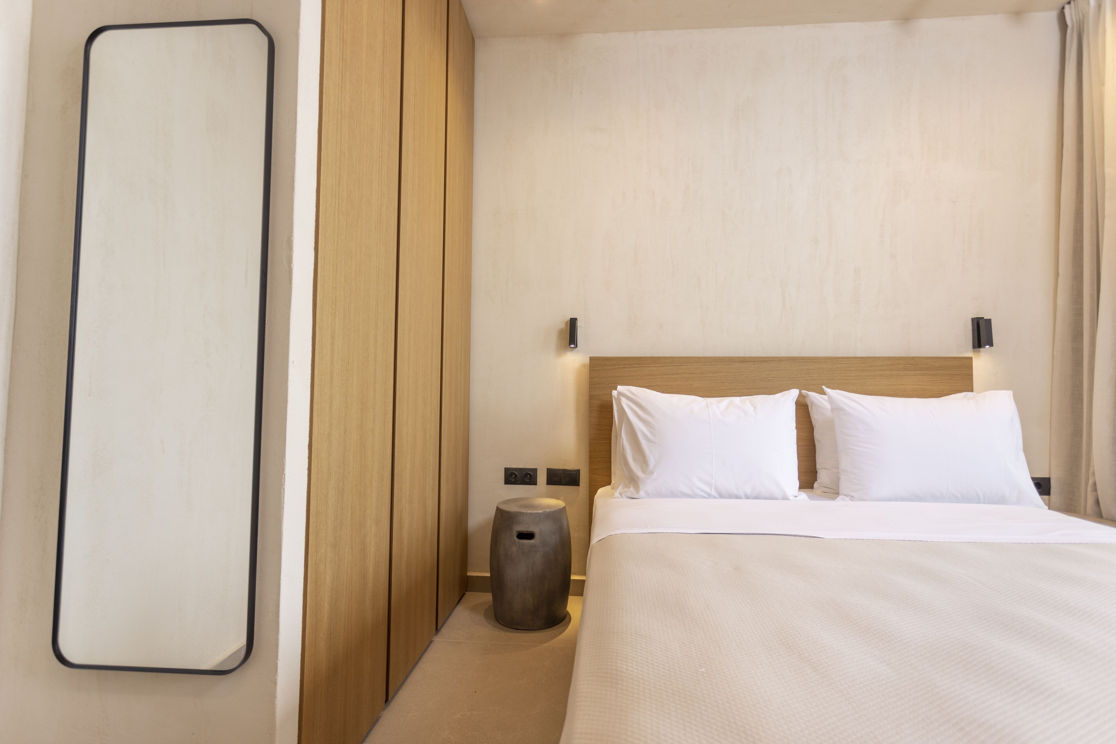 A modern hotel room with a large bed, wooden headboard, and a round nightstand.