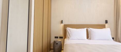 A modern hotel room with a large bed, wooden headboard, and a round nightstand.
