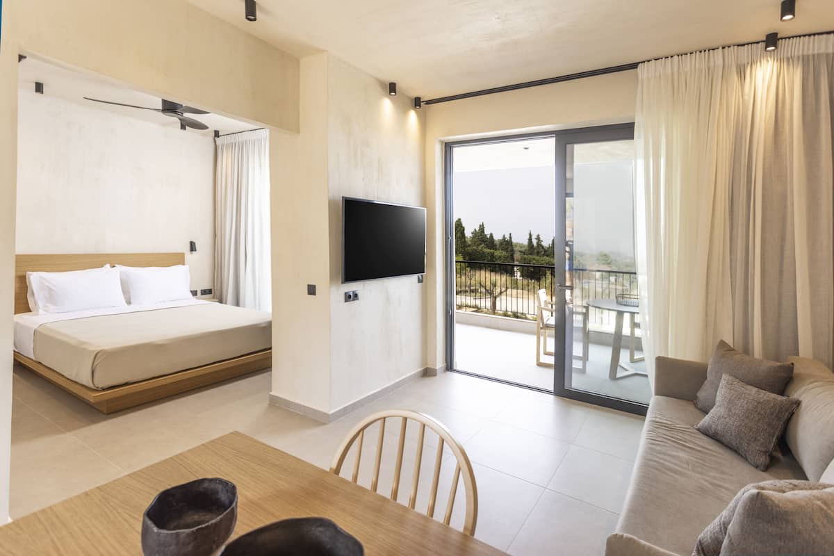 A modern hotel room with a bed, a flat-screen TV, a dining table, and a sofa.