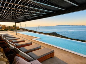 A poolside area with lounge chairs and a view of the sea. - ReGenesis Villas (Tinos)