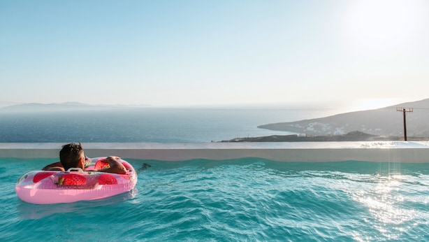 A person relaxing in a pool with a view of the sea and distant mountains. - ReGenesis Villas (Tinos)