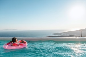 Una persona descansando en una piscina con vista al mar y montañas a lo lejos.