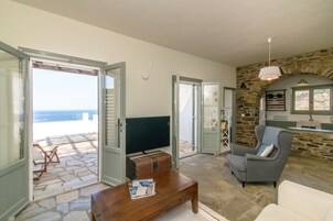 Un salón con chimenea de piedra, televisor y vistas al mar a través de puertas abiertas.