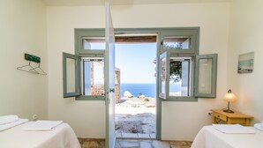A room with two beds, a stone floor, and a view of the sea through open windows. - ReGenesis Villas (Tinos)