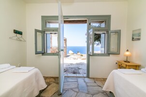Una habitación con dos camas, piso de piedra y vistas al mar a través de ventanas abiertas.