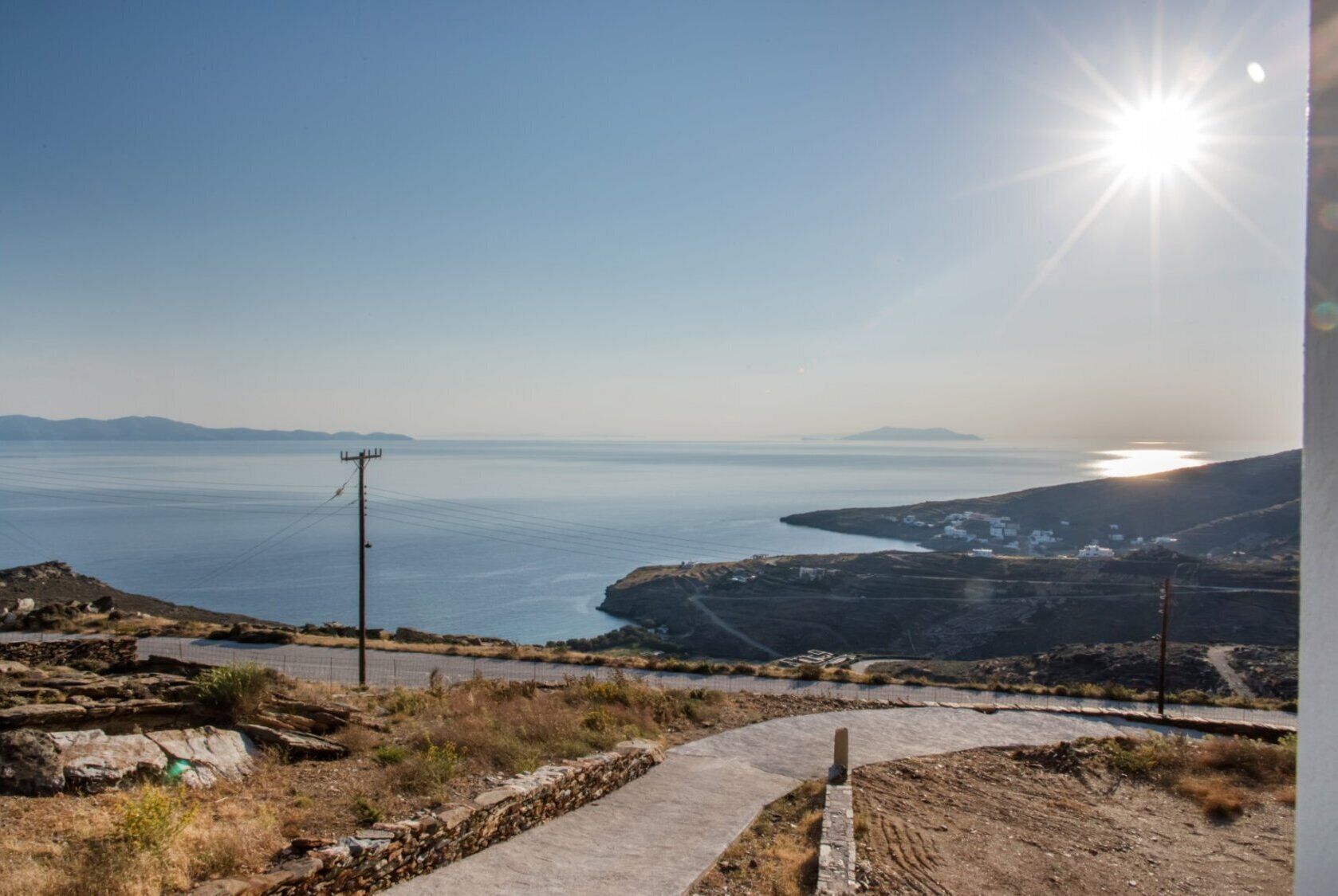A coastal landscape with a clear sky, a sunlit sea, and a distant view of a small settlement.
