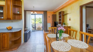 Une cuisine moderne avec des meubles en bois, un coin repas avec une table pour quatre personnes et un balcon offrant une vue sur la verdure.