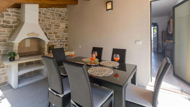 Un espace extérieur aménagé pour les repas, avec des chaises en osier et une cheminée en pierre.