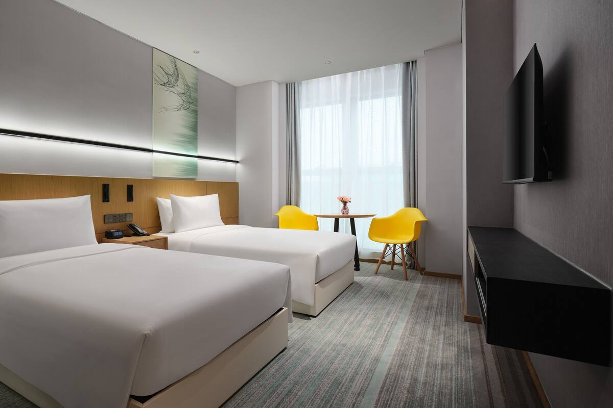 A hotel room with two beds, a desk, a chair, a TV, and a window with curtains.