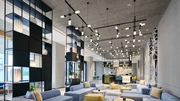 A modern interior with sectional sofas, a bar area, and a kitchen in the background. - Q-Box Hotel Shangqiu Expo Center (Shangqiu)