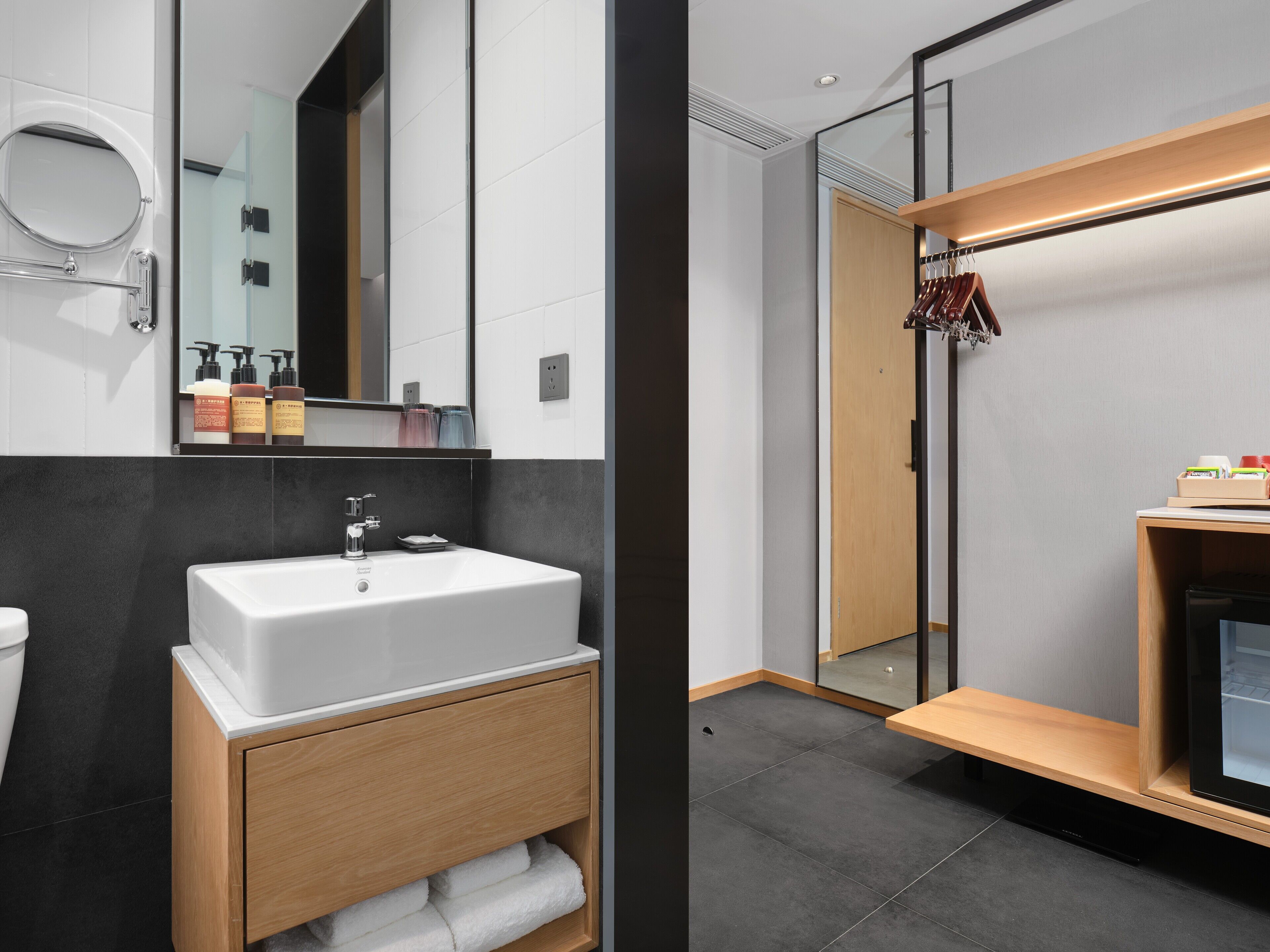 A modern bathroom with a white sink, dark tiles, and a wooden vanity.