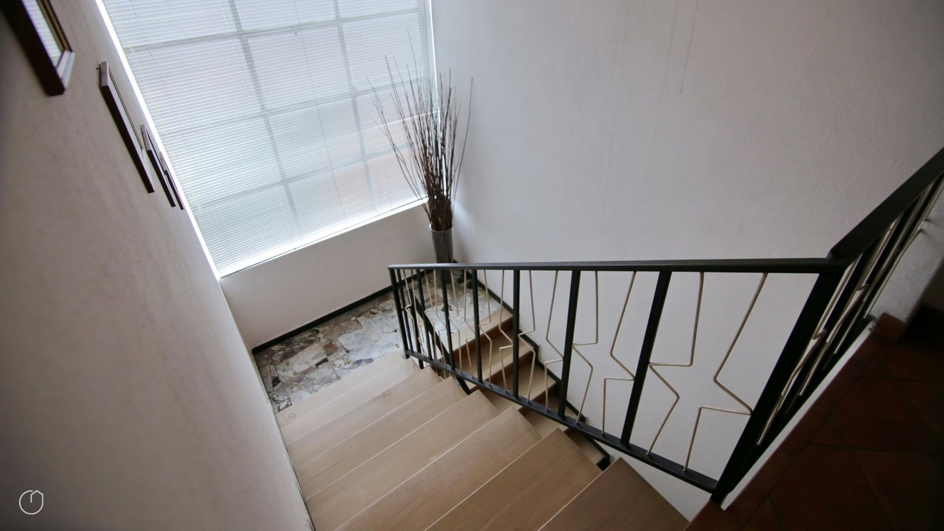 Un escalier avec une rampe en métal, des marches en bois et une fenêtre avec des stores.
