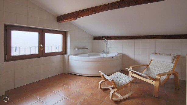 A bathroom with a bathtub, a rocking chair, and a window with a balcony view. - Italianway - Piazza Nuova 3 (Centro Valle Intelvi)