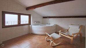 Un baño con bañera, una mecedora y una ventana con vistas al balcón.