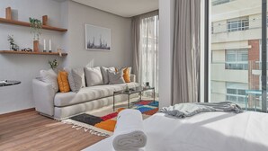 Ein modernes Hotelzimmer mit einer Couch, einem Couchtisch und einem Bett mit einem zusammengerollten Handtuch.