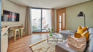 Ein modernes Wohnzimmer mit großem Fernseher, einer Couch, einem Couchtisch und Blick auf die Stadt durch große Fenster.