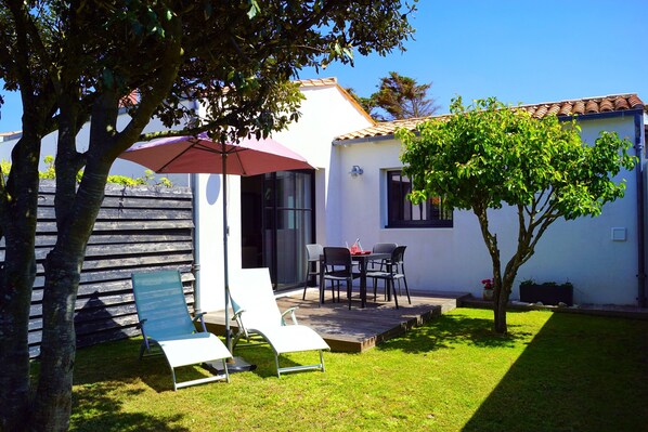Un patio con mobiliario exterior, una mesa pequeña y un paraguas rojo.