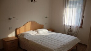 A bedroom with a wooden bed, two bedside tables, and a window with sheer curtains. - Two Bedroom Apartment (IDRO)