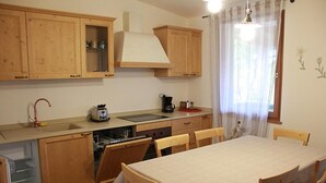 A kitchen with wooden cabinets, a sink, a stove, and a dining table with chairs. - Two Bedroom Apartment (IDRO)