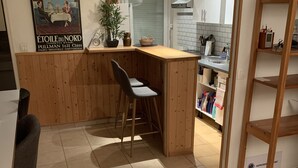 Moderni keittiö, jossa on puinen keittiösaareke, baarituolit, laattalattia ja juliste seinällä.