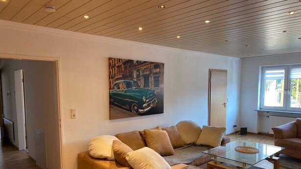 Una sala de estar moderna con un sofá, una mesa de centro de vidrio y un cuadro de un coche clásico en la pared.