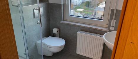 Ein modernes Badezimmer mit Duschkabine aus Glas, Toilette, Handtuchwärmer und Blick auf die Umgebung durch ein Fenster.