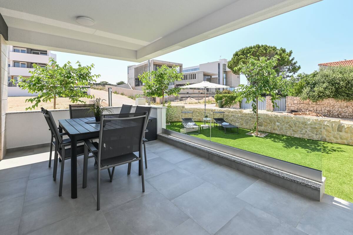 Un patio exterior con una mesa y sillas de comedor, un muro de piedra y vistas a un área verde y edificios al fondo.