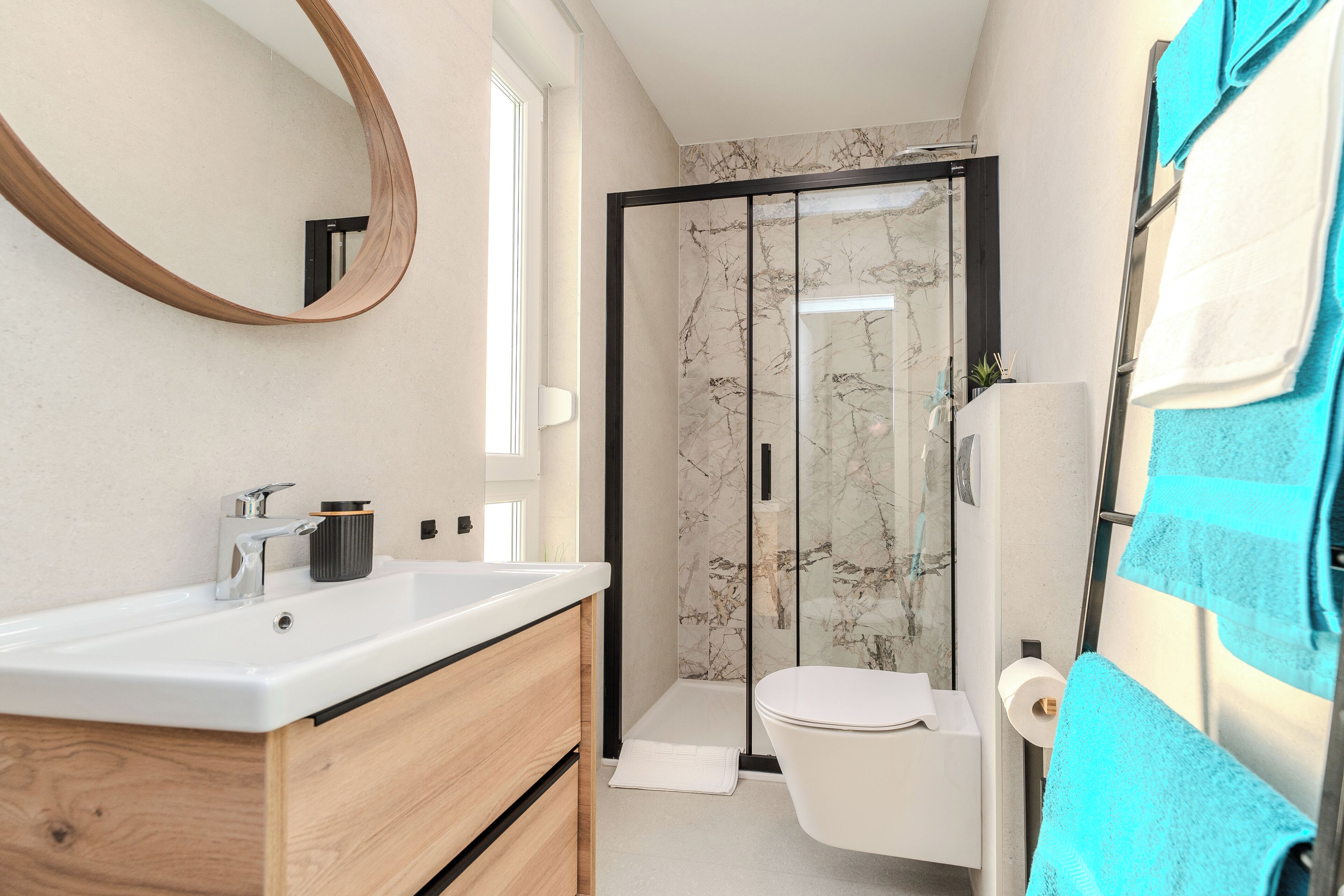 A modern bathroom with a wooden vanity, a glass shower enclosure, and a towel rack with a blue towel.