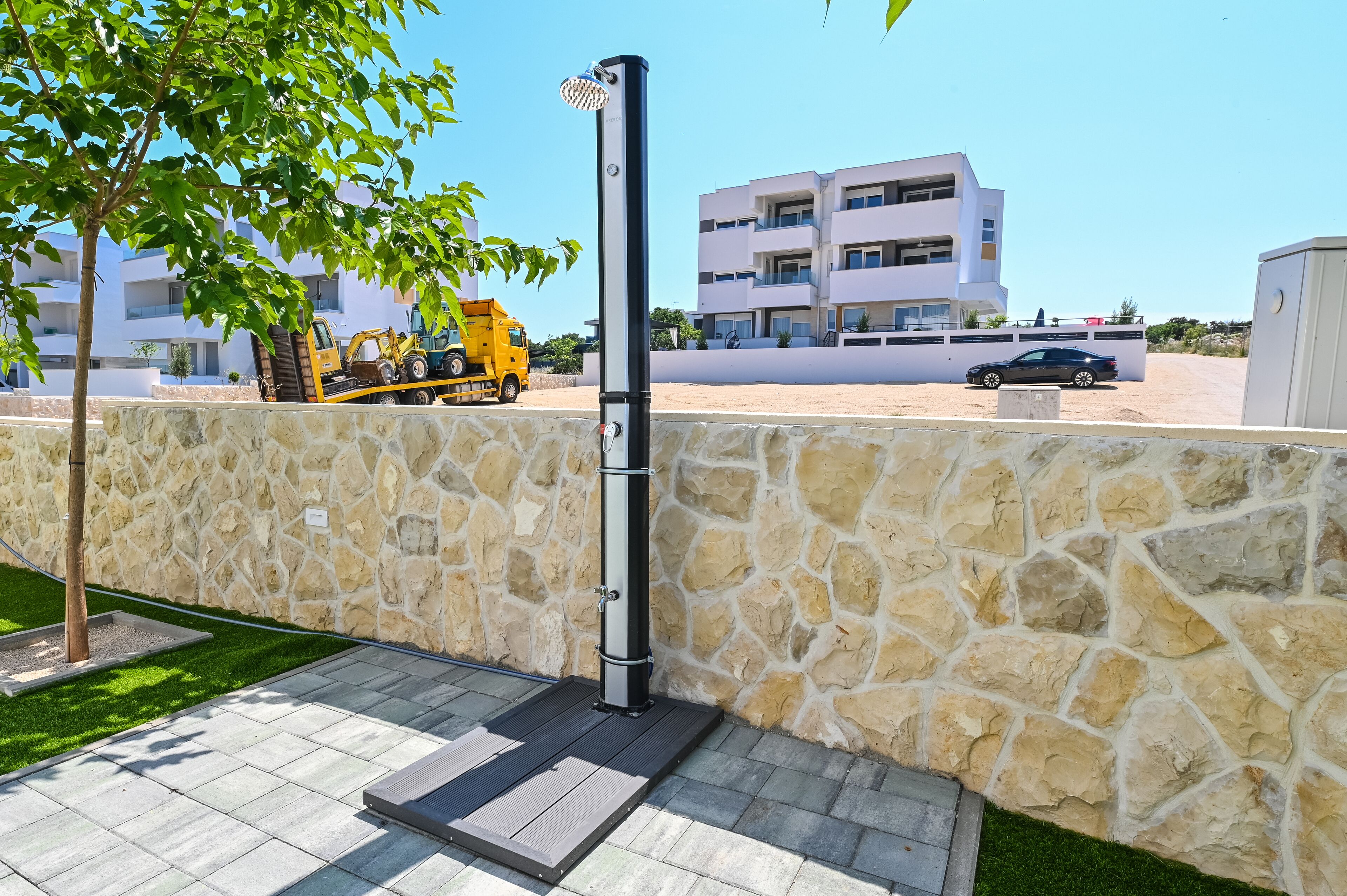 Un edificio moderno con un muro de piedra y un espacio pavimentado con estructura metálica.