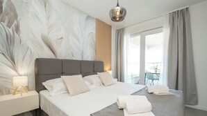 Camera d'albergo moderna con un letto grande, un comodino, una lampada, vista sull'esterno e un'ampia finestra con tende.
