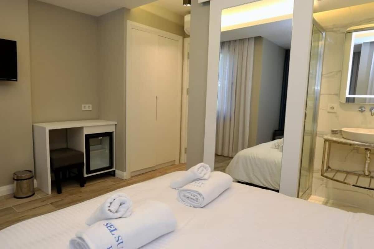 Una habitación de hotel con cama, escritorio, televisor, baño y toallas sobre la cama.
