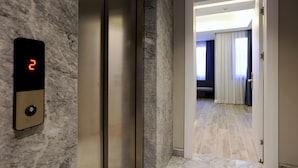 An elevator with a digital display showing the number 2, a marble wall, and a hallway leading to a room with a sofa and curtains.
