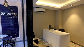 A hotel reception area with a reception desk, seating, and a large window with the hotel name.