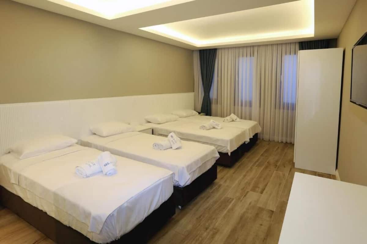 Habitación de hotel con tres camas individuales, cada una con ropa de cama y toallas blancas.