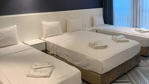 A hotel room with two single beds, a large window with curtains, and a dark accent wall.