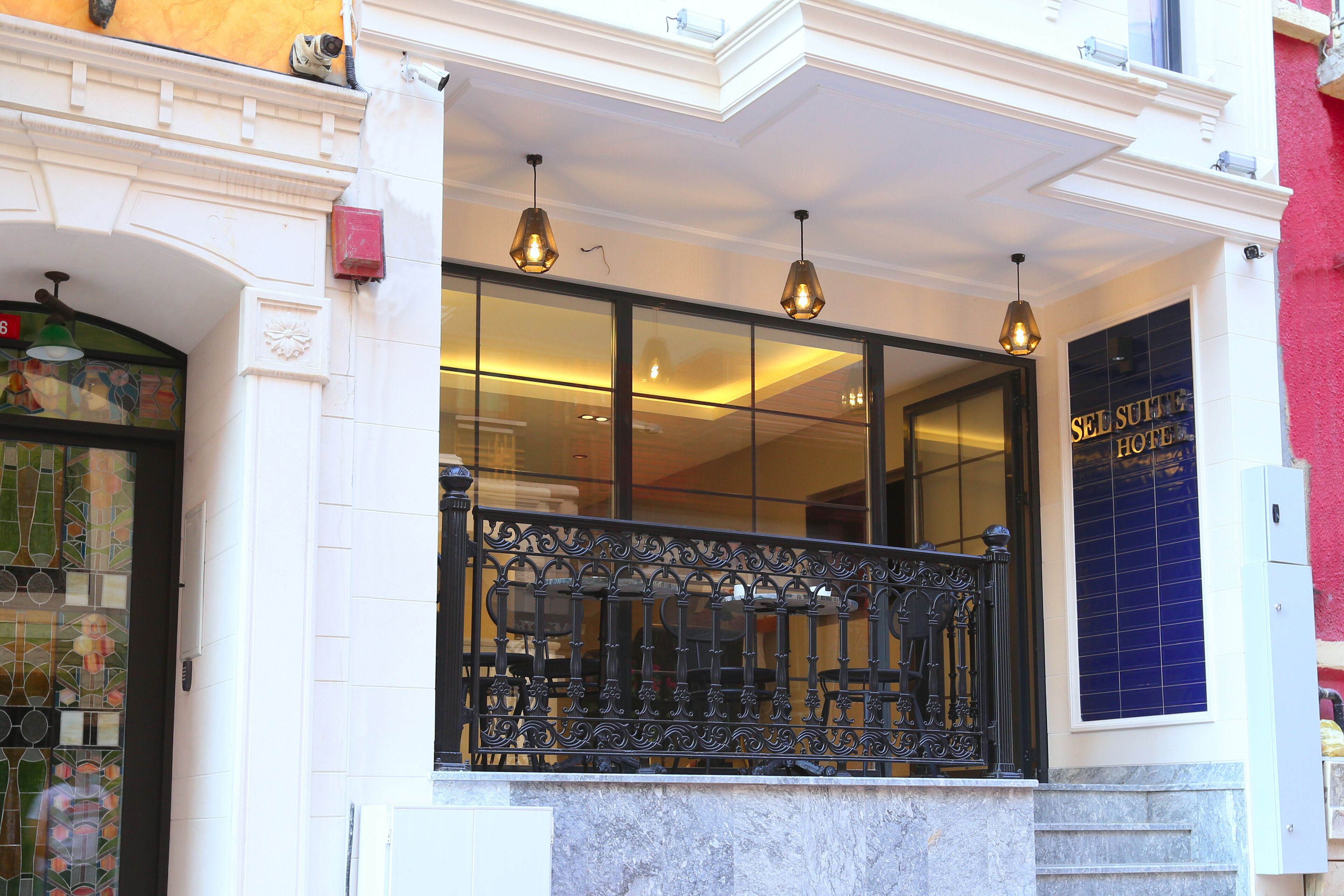 Entrada de un hotel con fachada de vidrio, un balcón con barandilla de hierro forjado y un cartel que dice "SEL SULTAN HOTEL".