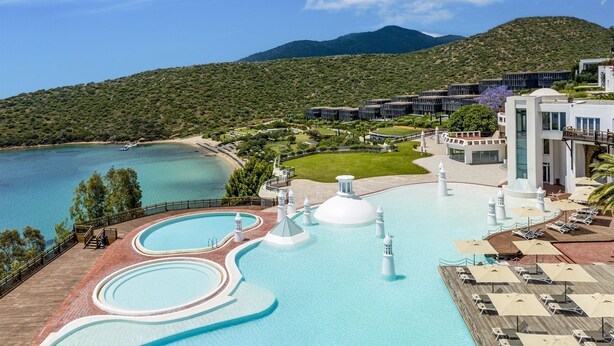 Ein Resort mit großzügigem Poolbereich, inklusive Wasserrutsche und mehreren Springbrunnen, umgeben von üppiger Vegetation und einer Bergkulisse.
