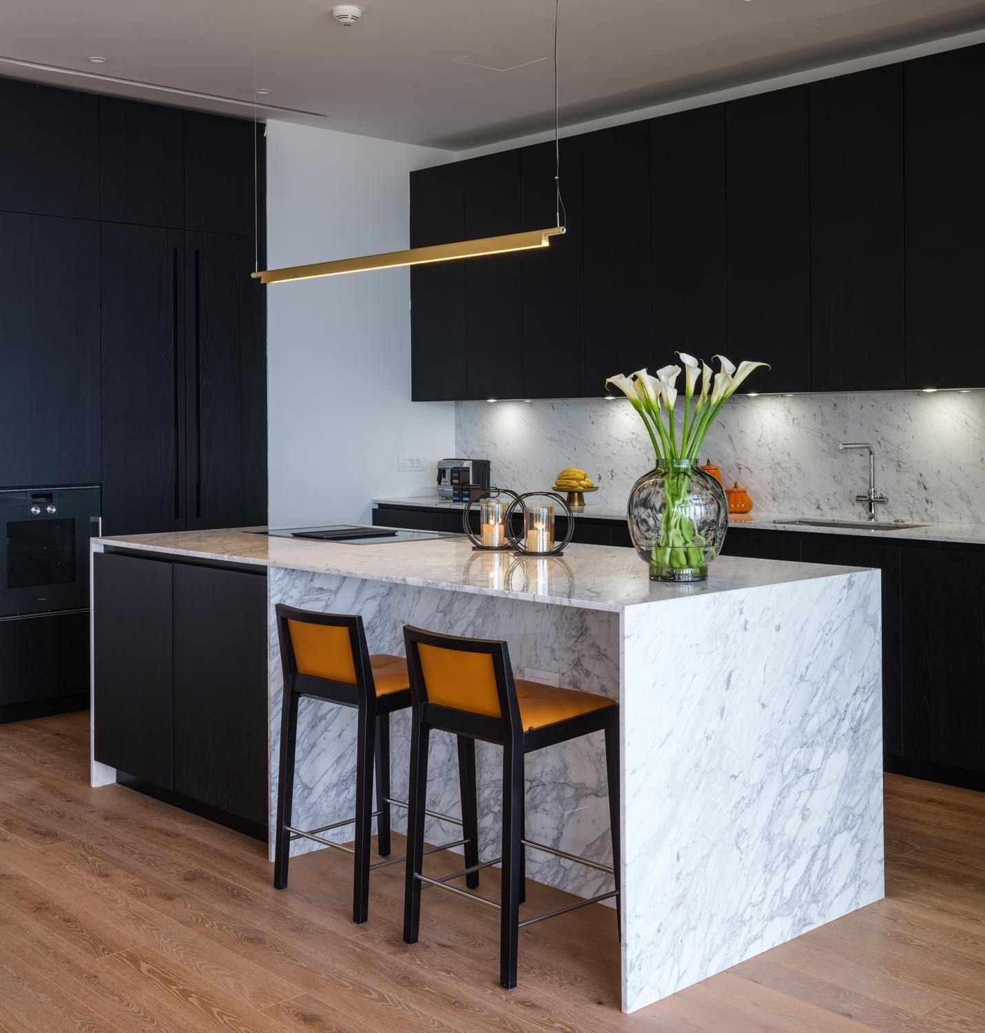 A modern kitchen with a marble island, dark cabinetry, and two bar stools.