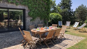 Un área de comedor al aire libre con un patio de piedra, sillas de madera y una mesa preparada para cuatro personas.