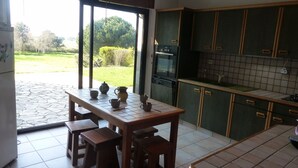 Una cocina con una mesa de comedor, taburetes, un refrigerador, un lavavajillas y un amplio ventanal con vistas a un jardín.