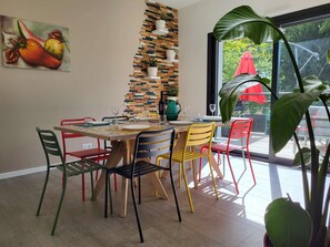 Un comedor con mesa de madera, sillas coloridas, un cuadro de frutas en la pared y una planta en la esquina.