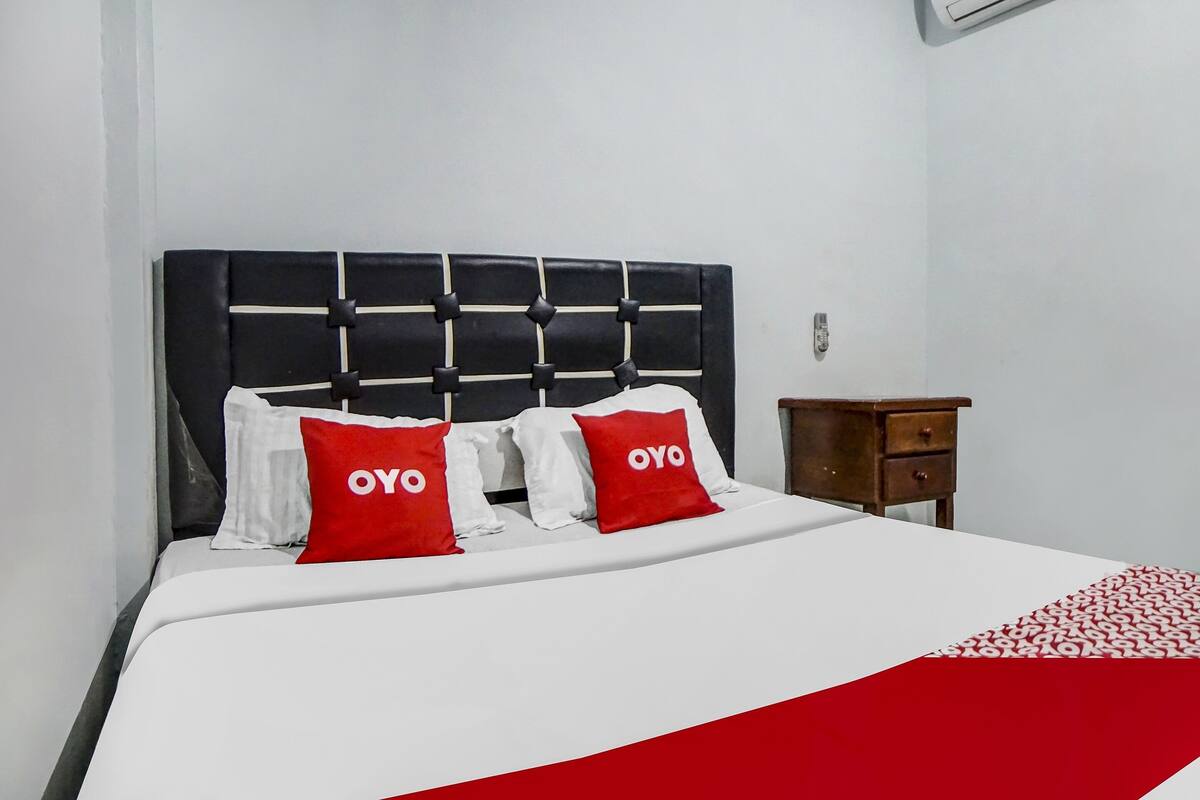A neatly made bed with a black headboard, two red pillows with "OYO" text, and a white bedspread.
