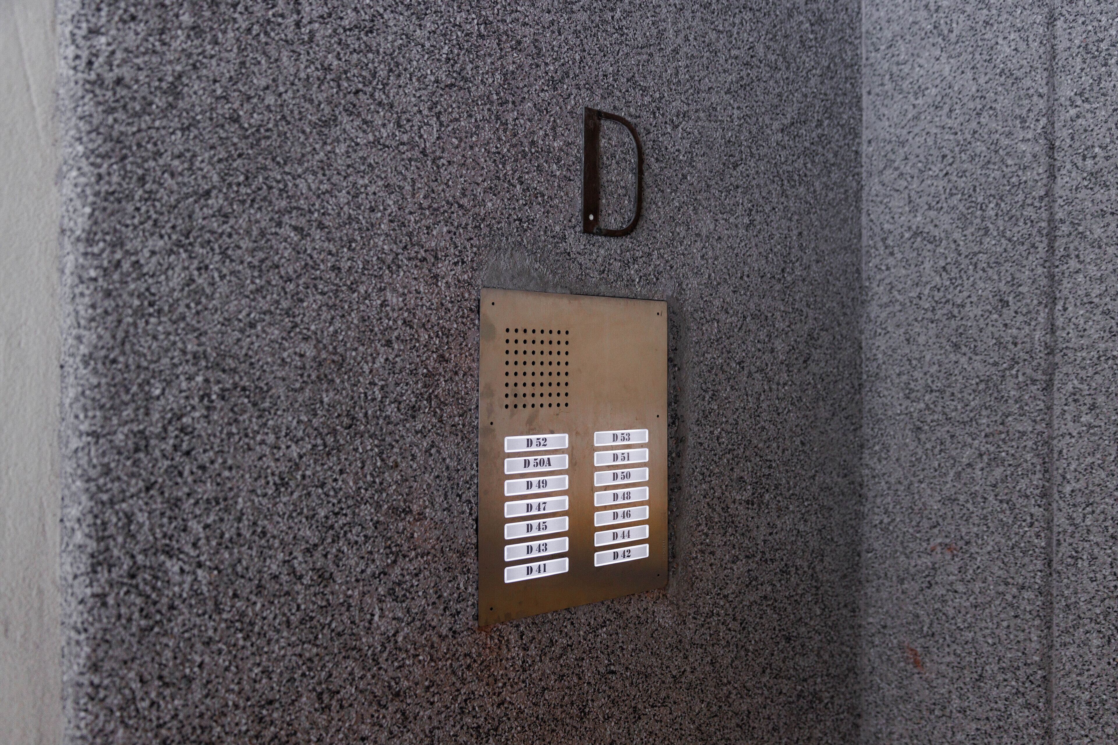Een metalen bedieningspaneel van een lift met gekleurde knoppen tegen een structuurwand.