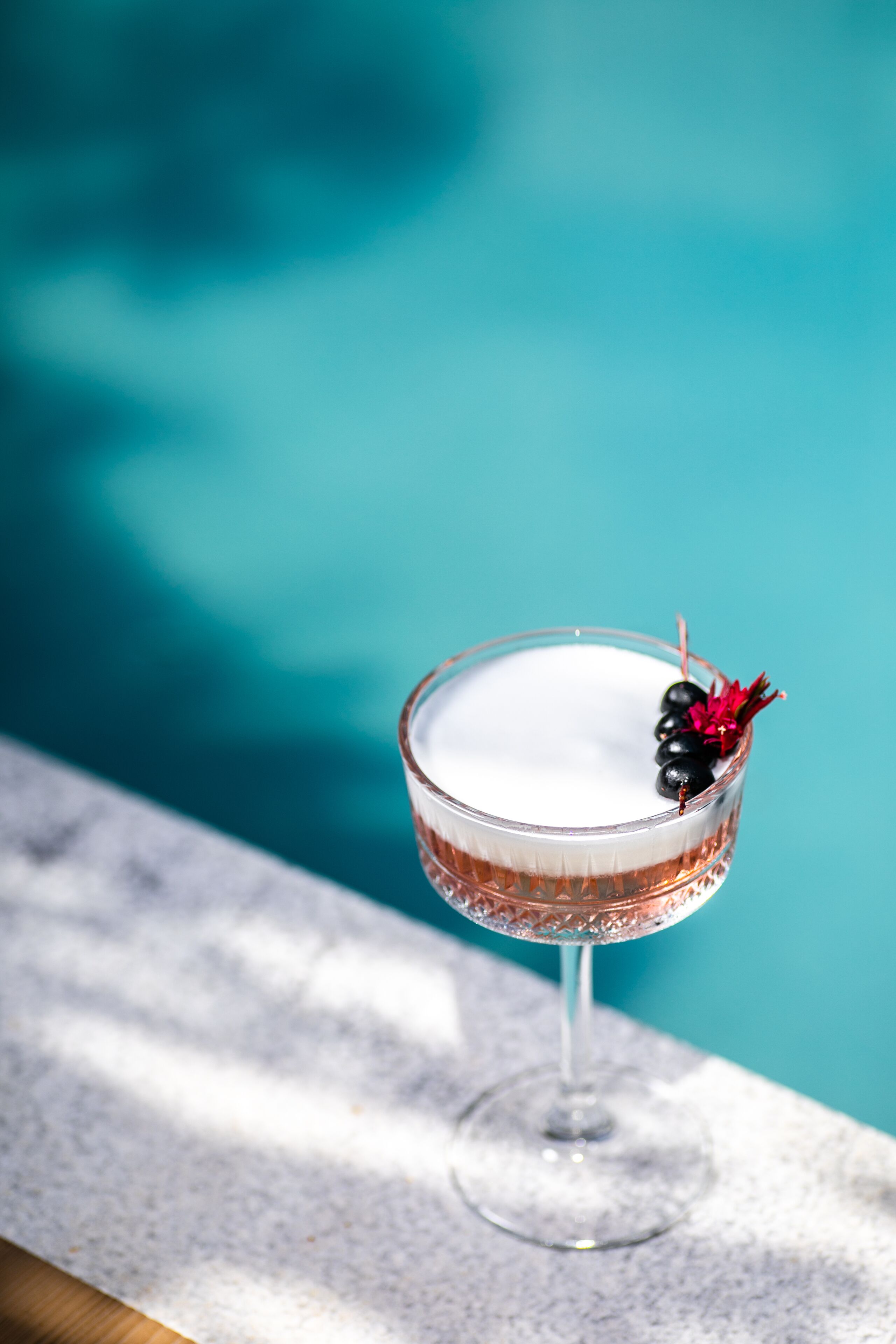 A cocktail glass with a decorative garnish on a marble surface near a pool.