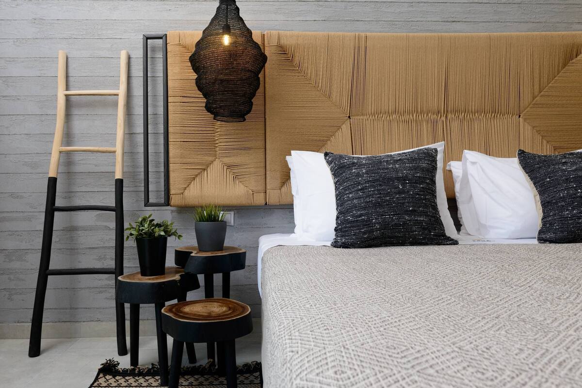 Quarto bem organizado com cama, almofadas, escada, pequena mesa com planta e luminária pendente.