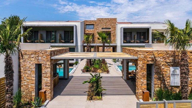 A modern hotel with a central pool, stone facade, and outdoor seating areas. - Soho Exclusive Suites (Thasos)