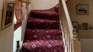 A staircase with a patterned carpet, wooden handrail, and a wall with framed pictures and a tapestry. - Dál Riada B&B (Carrick)